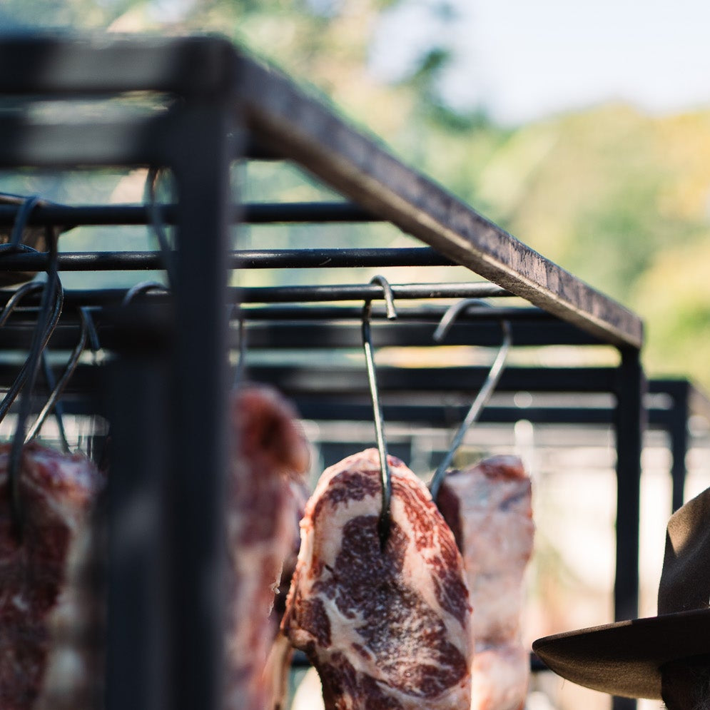 Raw meat hanging on hooks outdoors on Terra Grills Argentinian style BBQ