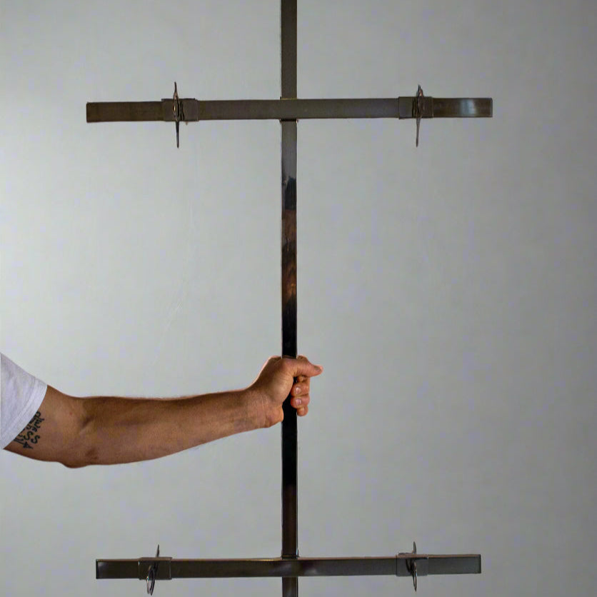 Person holding a large metal cross against a plain background. Traditional Argentinean Asado Cross for slow-roasting whole animals over open fire