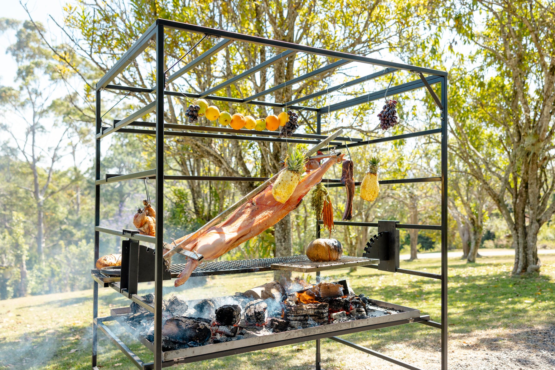 Outdoor Terra Grills Argentinian style barbecue grill with various food items on a metal stand in a forest setting. 