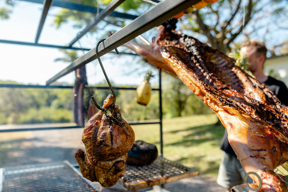 Two roasted chickens hanging on hooks over Terra Grills Portico Argentinian Style BBQ